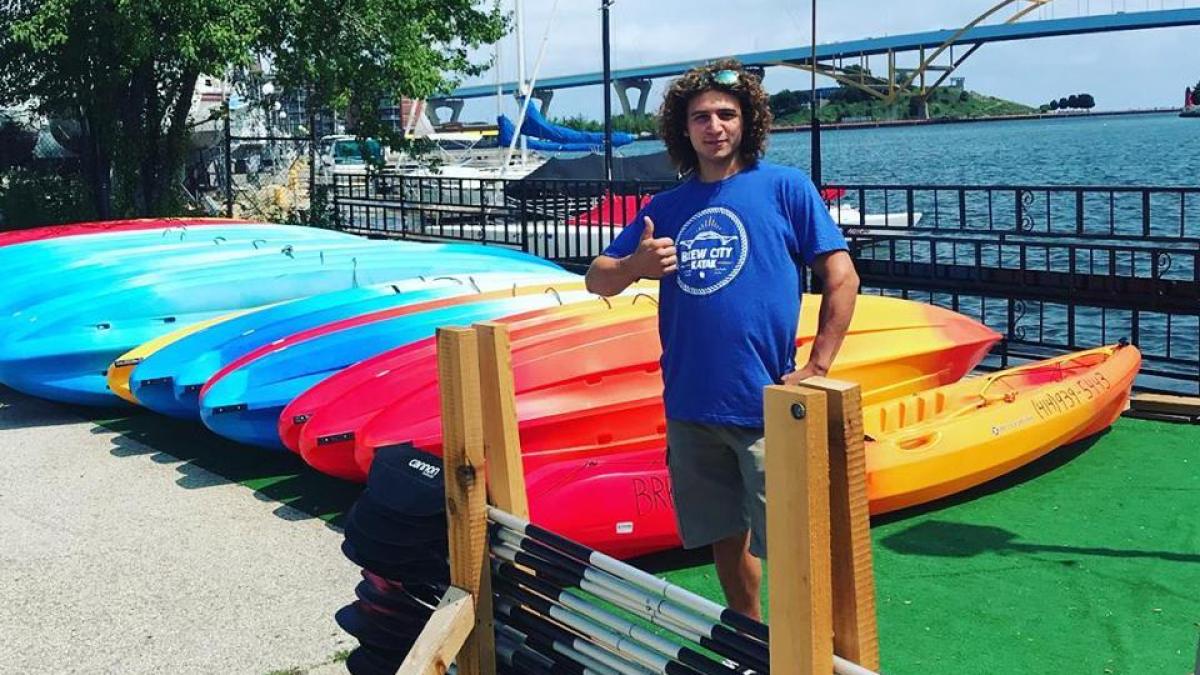A staff member giving the thumbs up for our kayaks. He is smiling in front of a row of single and double kayaks ready to go on Lake Michigan