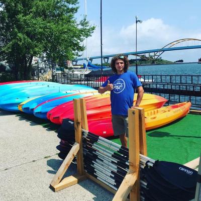 A staff member giving the thumbs up for our kayaks. He is smiling in front of a row of single and double kayaks ready to go on Lake Michigan