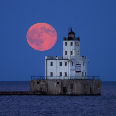 A pink full moon in a deep blue sky hovering over a white house