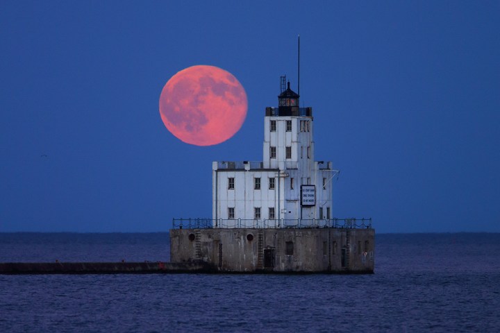 A pink full moon in a deep blue sky hovering over a white house
