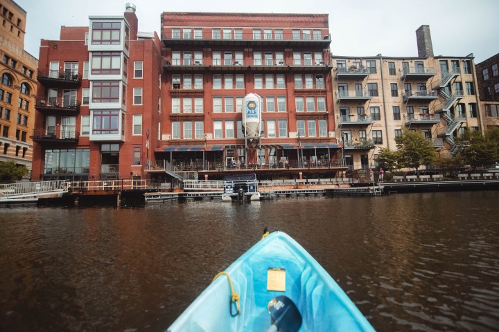 The nose of a kayak pointing at a red building with a sign that reads MKE Ale House