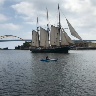 A kayaker peering at an old time ship with huge sails. A huge bridge is in the background.