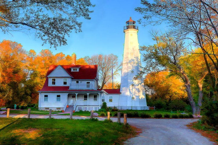 A white lighthouse with a red rooftop in front of fall foliage trees
